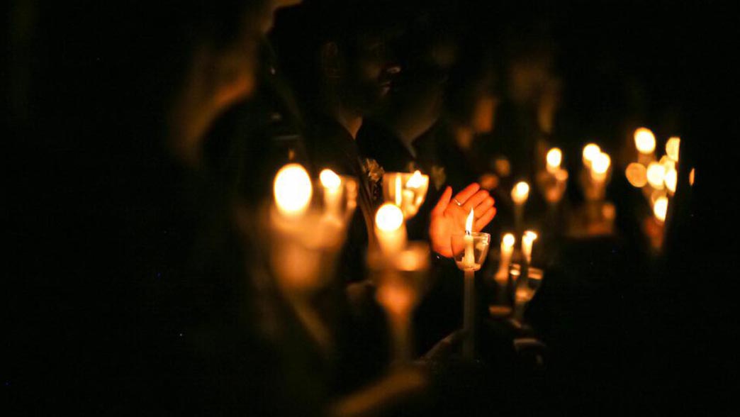 Many people in the dark holding lit candles